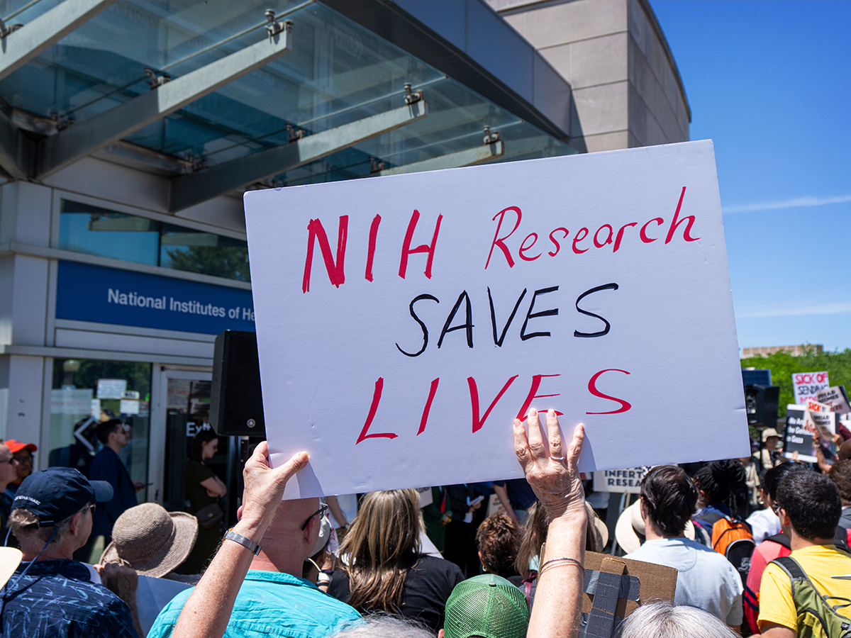 Activists at a rally outside the National Institutes of Health in Bethesda, Md., on May 10, 2025. An activist holds a sign reading "NIH research saves lives."